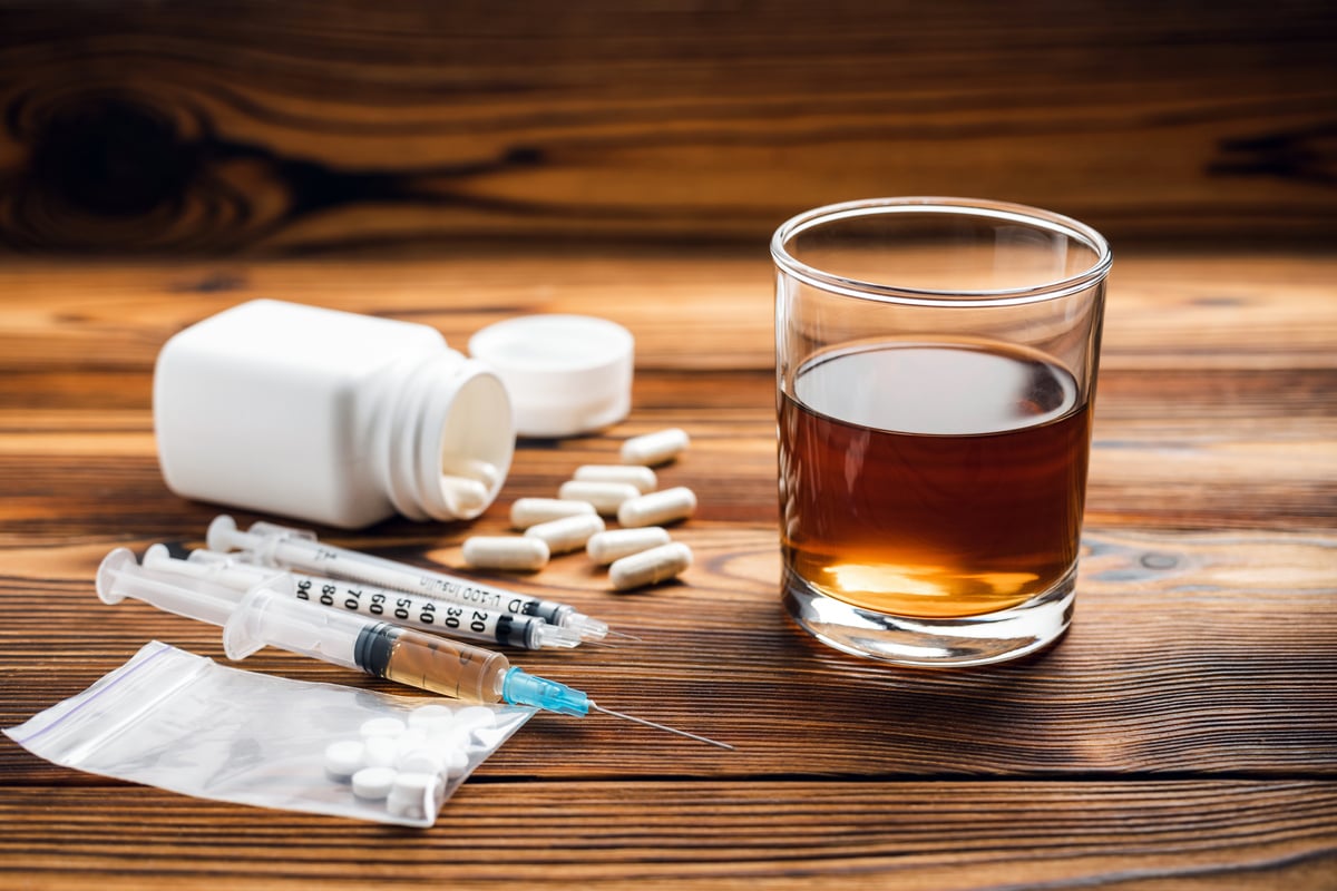 Glass with alcohol drink, whisky or brandy, white pills, syringe with a drugs dose, narcotic in transparent bag on a wooden table. Concept of addiction and bad habits